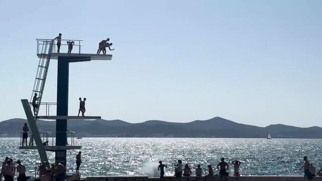silhouette group of people having fun jumping off diving platform into water outdoors at the beach in Zadar, Croatia