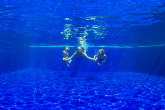 Happy family - mother, baby son, daughter in goggles swim, dive in pool with fun - jump deep down underwater. Healthy lifestyle, people water sport activity, swimming lessons on holidays with kids