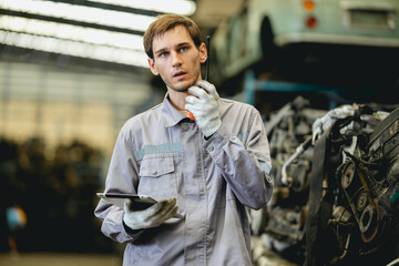 White man technician checking used car damaged engine block at scrap yard warehouse recycle area...