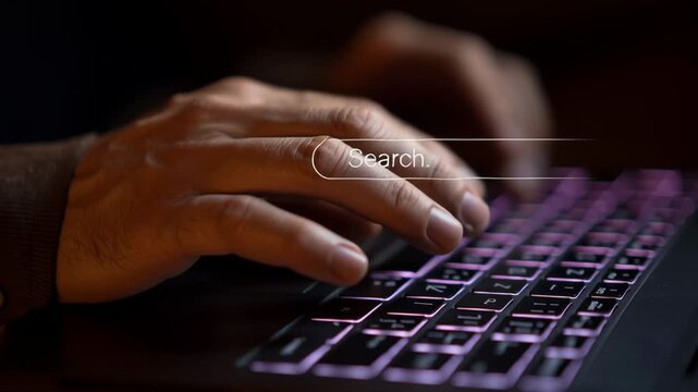 Searching online with a laptop, close-up view of hands typing on keyboard in a dark environment