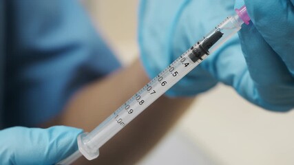 A close-up of a doctor's hands in blue protective gloves filling a syringe with medication. A nurse fills a syringe with a vaccine from an ampoule.