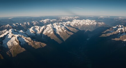Aerial view of snow-capped mountain peaks under a clear blue sky, casting shadows