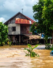 Two-story wooden house, elevated and partially flooded in a muddy river
