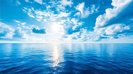 A serene landscape with a clear blue sky filled with fluffy white clouds above calm reflective water shimmering under br