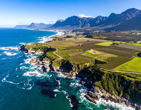 Aerial panorama capturing rugged coastline, fields, a town, and mountains under a clear sky - Powered by Adobe