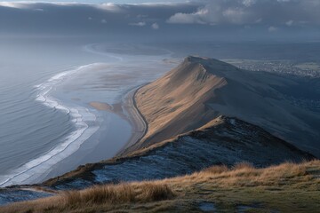 Rugged coastal mountain ridge overlooking ocean waves and tidal flats under dramatic sky.