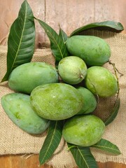 Fresh green mangoes with leaves arranged on burlap fabric, showcasing tropical fruit in a natural rustic setting.
