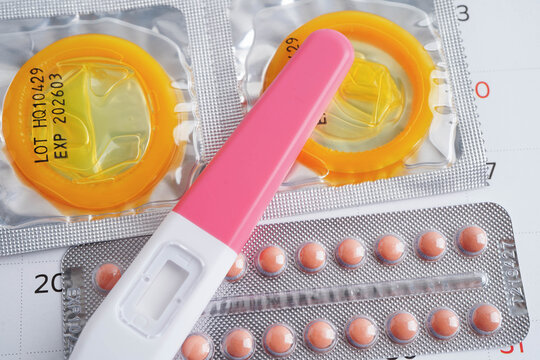 Pregnancy test with birth control pills and condom for female on calendar, ovulation day.