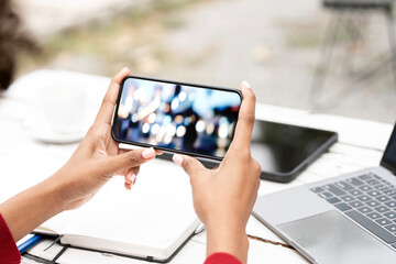 A person holds a smartphone horizontally to capture a moment, with bokeh lights in the background.