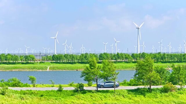 An electric car is driving outdoors, with a spinning windmill in the distance. Green new energy vehicle video
