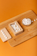 White vitamin pills in wooden bos and glass bowl from above on a wooden desk on orange bakcground.