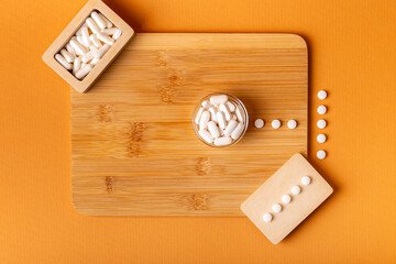 White vitamin pills in wooden bos and glass bowl from above on a wooden desk on orange bakcground.