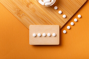 White vitamin pills in wooden bos and glass bowl from above on a wooden desk on orange bakcground.