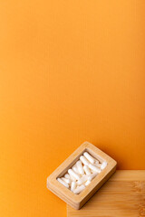 Nutritional supplements, vitamins and minerals. White vitamin pills in wooden box l from above on a wooden desk on orange background. Healthy lifestyle