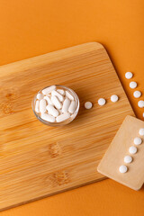 White vitamin pills in wooden bos and glass bowl from above on a wooden desk on orange bakcground.