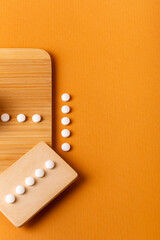 Nutritional supplements, vitamins and minerals. White vitamin pills from above on a wooden desk on orange background. Healthy lifestyle