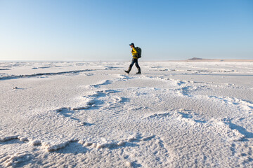 Man traveler with backpack walking on the salt flat at sunrise. Baskunchak lake, Russia