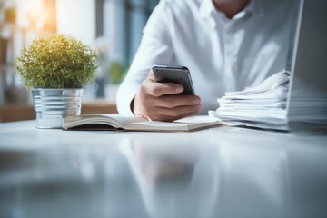 Businessman Using Smartphone and Laptop in Modern Office Environment with Documents and Plant on Desk