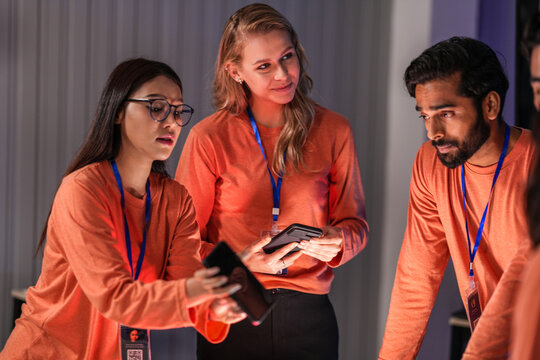 A diverse team of young innovators in a tech lab presents a new smartphone prototype, enthusiastically brainstorming its next-generation design and user interface for a future product launch.