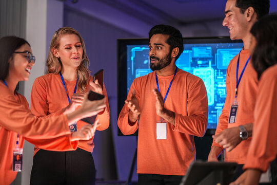 A diverse team of young innovators in a tech lab presents a new smartphone prototype, enthusiastically brainstorming its next-generation design and user interface for a future product launch. - Powered by Adobe