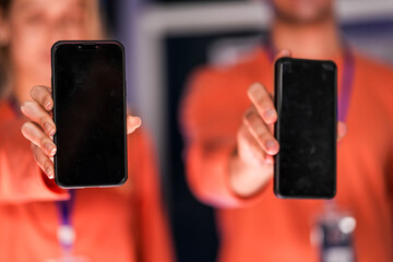 A diverse man and woman present smartphones with blank screens, perfect for a new app mockup. A showcase for mobile communication technology in a modern office setting.