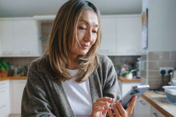 Woman in a kitchen using a smartphone while preparing for a meal in a cozy, modern space