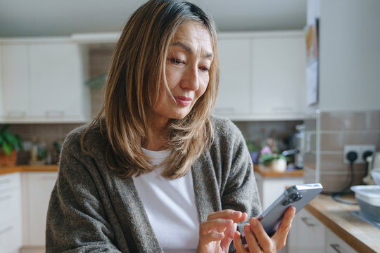 Woman in a kitchen using a smartphone while preparing for a meal in a cozy, modern space - Powered by Adobe