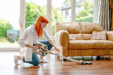 Woman cleaning living room with vacuum cleaner during daylight in cozy home environment
