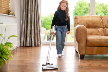 Young girl helps with house chores by vacuuming the living room on a sunny day