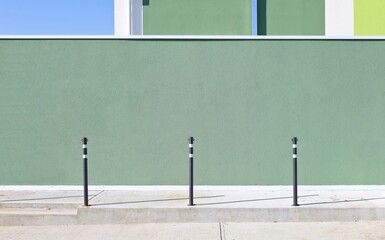 Black safety bollards on sidewalk with green plaster wall on behind. MInimal urban background for copy space.