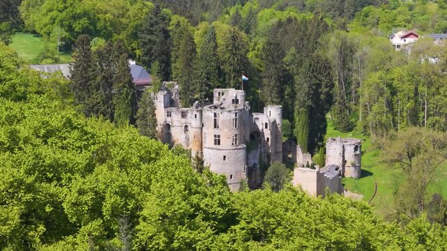 medieval castle beaufort les ch teaux de displays green cover old site town below another hill tall trees flag atop building from forward drone shot luxembourg 