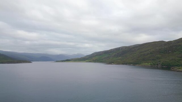 Expansive aerial view along calm Loch Broom with distant Highland mountains under grey cloud