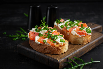 Salmon sandwiches, salted fish,  cream cheese and green onion on wooden background. Healthy breakfast with salmon toasts