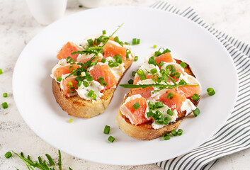 Two open sandwich, toast with salmon, cream cheese, green onions for healthy breakfast on white plate.