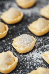 Fresh uncooked cappelletti sprinkled with flour on black stone background