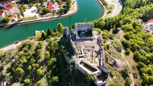 Aerial flight over Kurjaković Fortress with a direct look inside, then onward to the green Zrmanja River and the town of Obrovac surrounded by lush nature.
