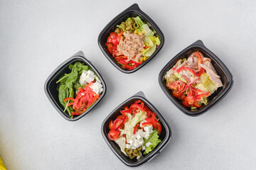 Mixed salads with fresh vegetables meat cheese and greens in black containers for restaurant delivery or meal prep concept