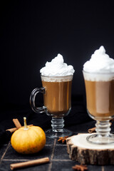 Pumpkin spice drinks with whipped cream and cinnamon sticks on a dark table background
