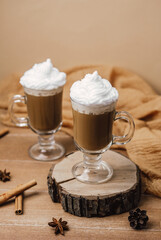 Two warm drinks with whipped cream on a rustic wood slice with cinnamon sticks and star anise
