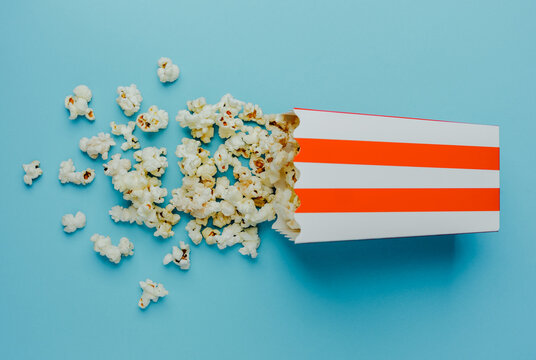 Popcorn spilling from a striped box on a blue background during a snack time - Powered by Adobe
