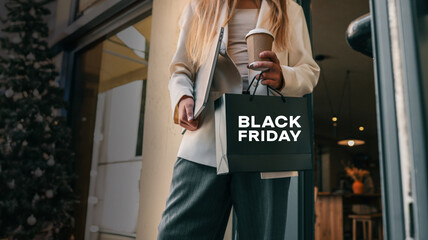 Woman holding a Black Friday shopping bag and a coffee cup, ready for deals