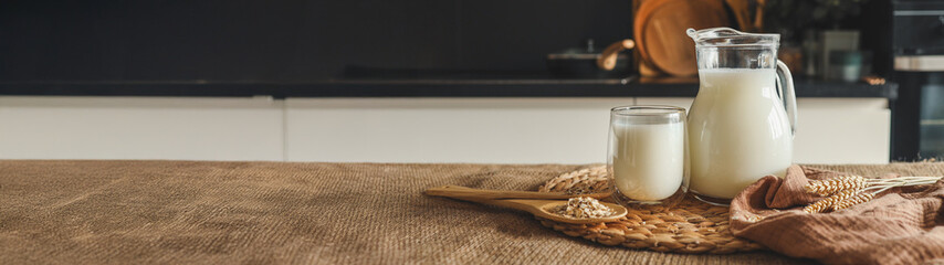 Fresh oat milk in a glass and pitcher on a rustic wooden table