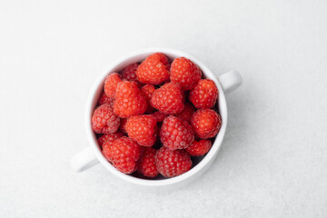 Raspberries in white bowl on light surface for organic food or vegan diet concept
