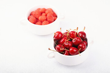 Cherries bowl and raspberries cup on white for minimalist food styling or healthy pairing concept