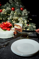 A person is cutting a festive cake adorned with a red flower, surrounded by christmas holiday decorations, glowing lights, and a joyful atmosphere perfect for winter celebrations.