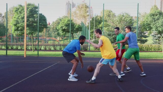 Determined male basketball defender making illegal player contact, committed personal foul against African American ball carrier, going for steal but hitting players hand during game on outdoor court
