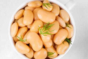 Butter beans in white bowl with dill on white background for nutrition, vegan food or healthy meal concept