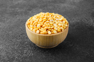 Yellow split peas in wooden bowl on stone background for vegan protein, clean ingredient or rustic food concept