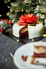 A beautifully arranged plate holds a slice of decadent layered cake, showcasing red velvet and cream cheese layers, surrounded by twinkling lights and holiday decor.