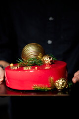 A beautifully crafted red cake, topped with a golden ornament and festive greenery, is being held by a person, perfect for holiday festivities and celebrations.